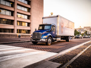 Kenworth T280 medium-duty box truck operating in a downtown commercial delivery environment