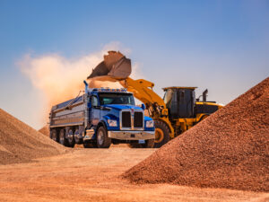 Blue Kenworth T880S dump truck being loaded by a wheel loader at an aggregate operation.