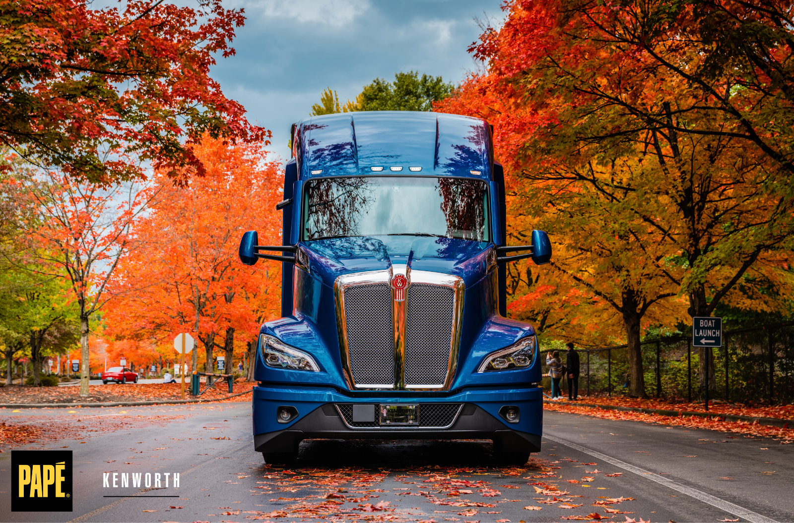 Blue Kenworth truck parked on a road surrounded by colorful fall foliage.
