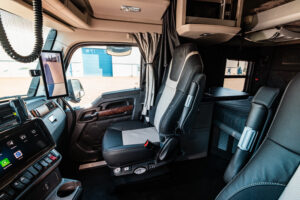 Interior of a Kenworth semi-truck sleeper cab featuring premium seating, a sleeping area, dashboard controls, and a digital side-view mirror display.